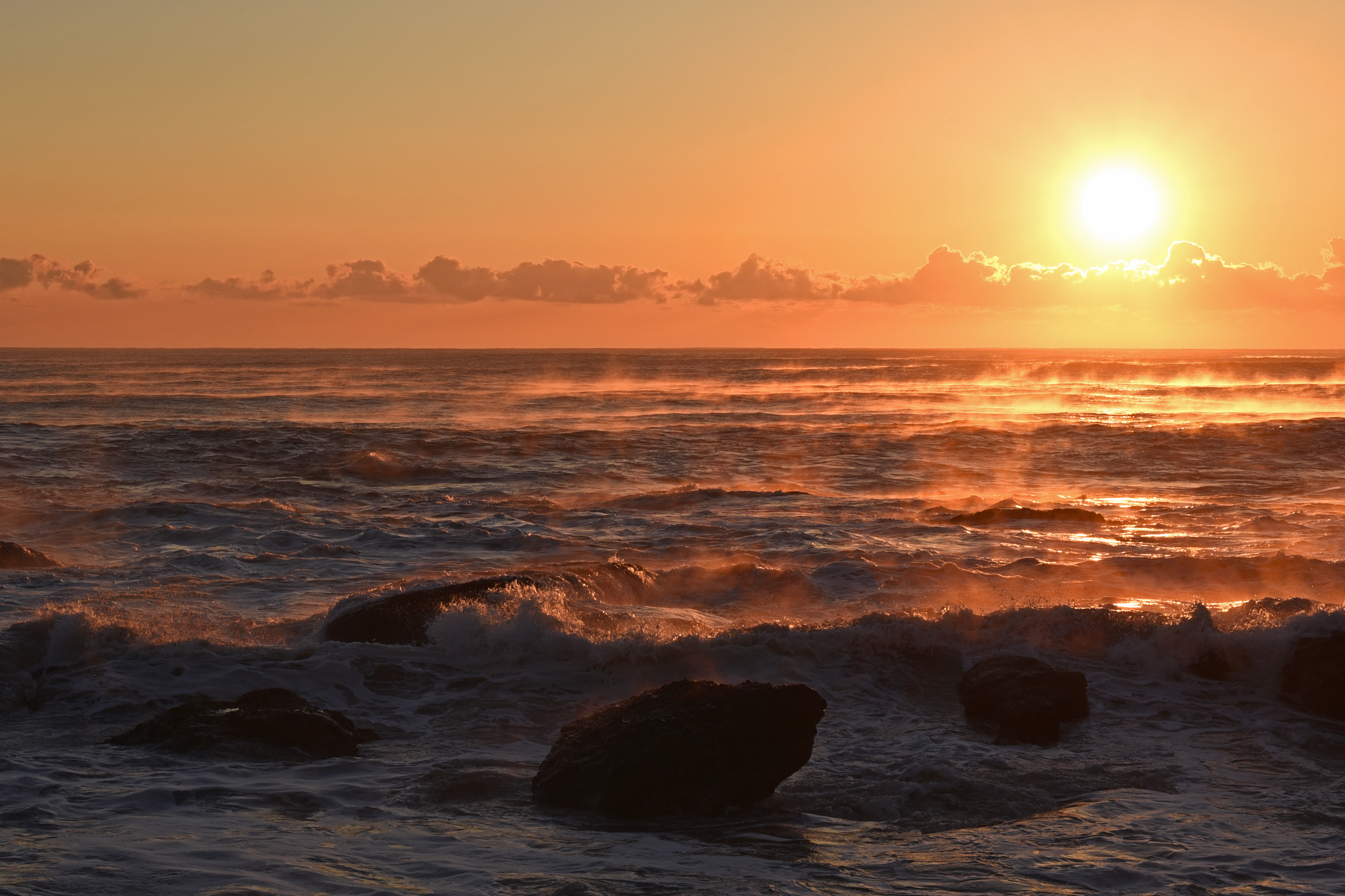 夕日に照らされた波しぶきをあげる海